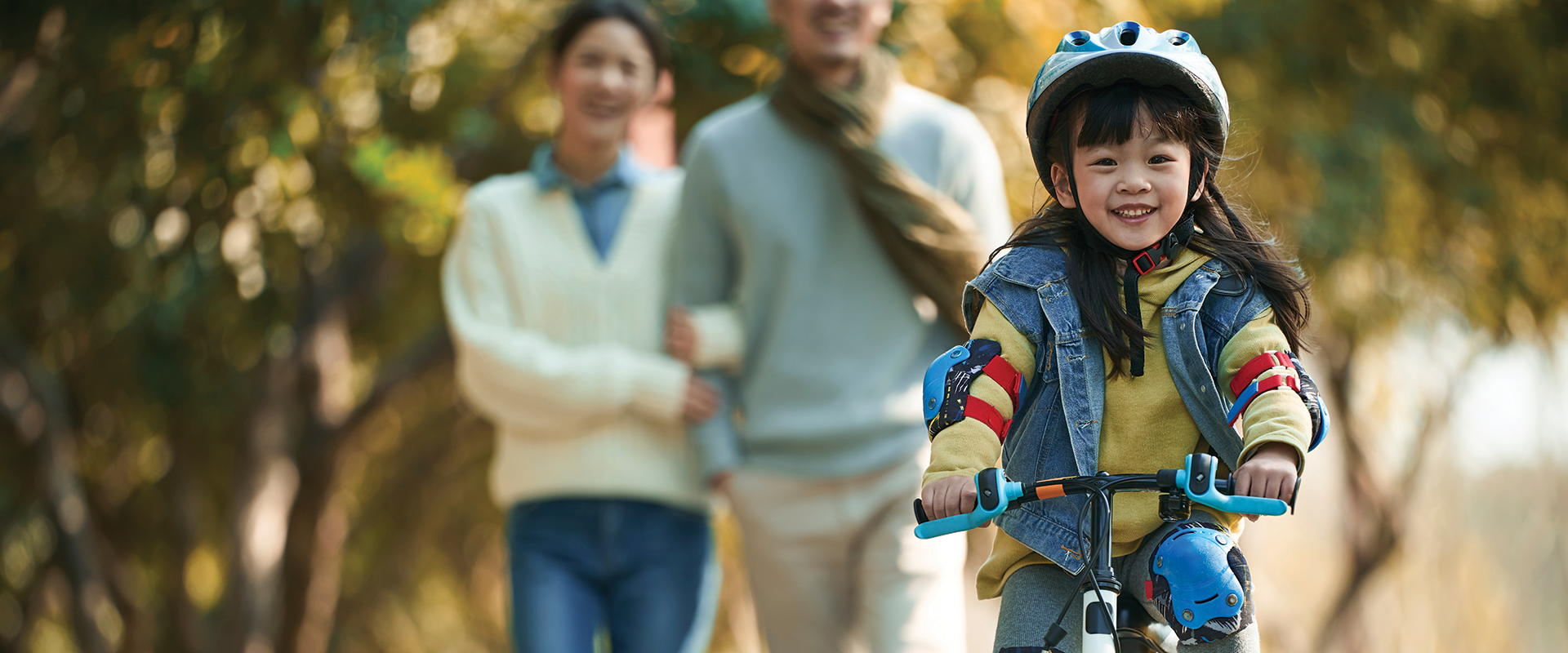 A girl riding bike with her family walking in the background