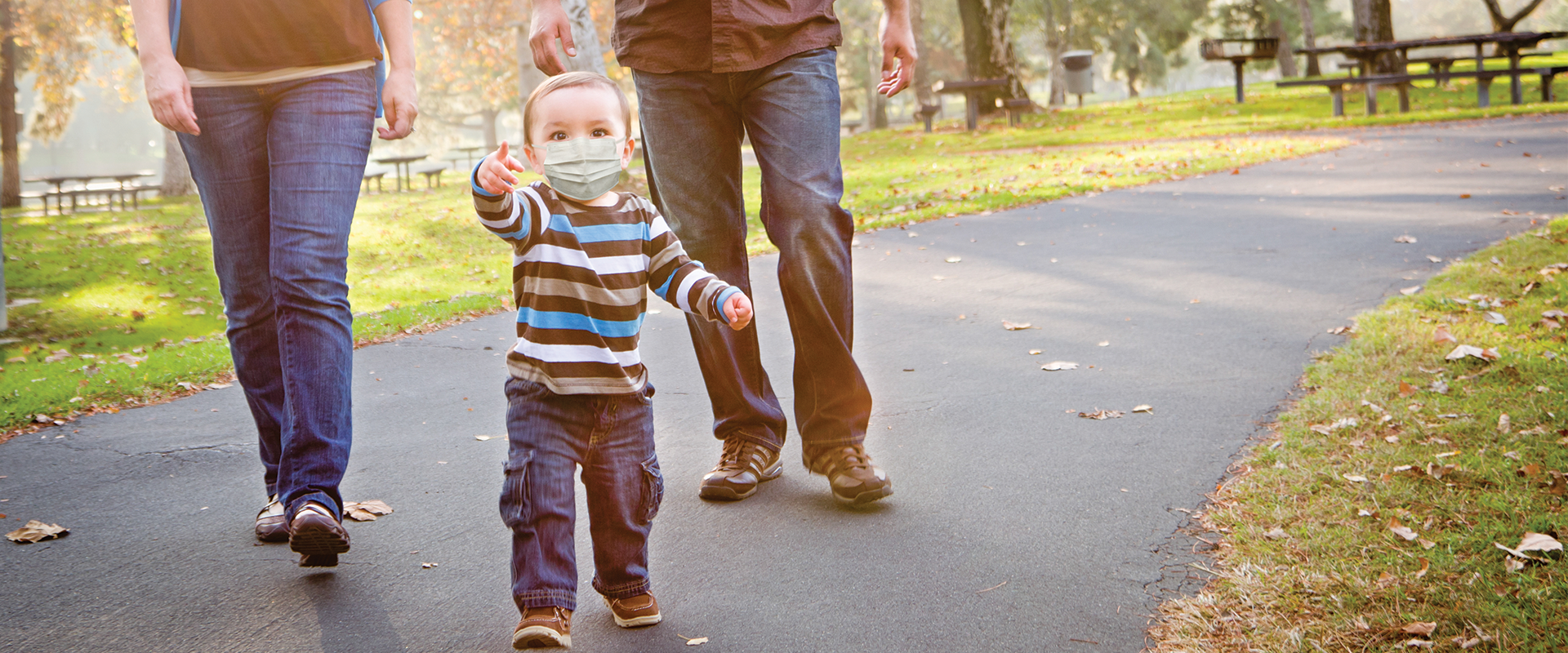 A toddler and parents with masks on walking in a park