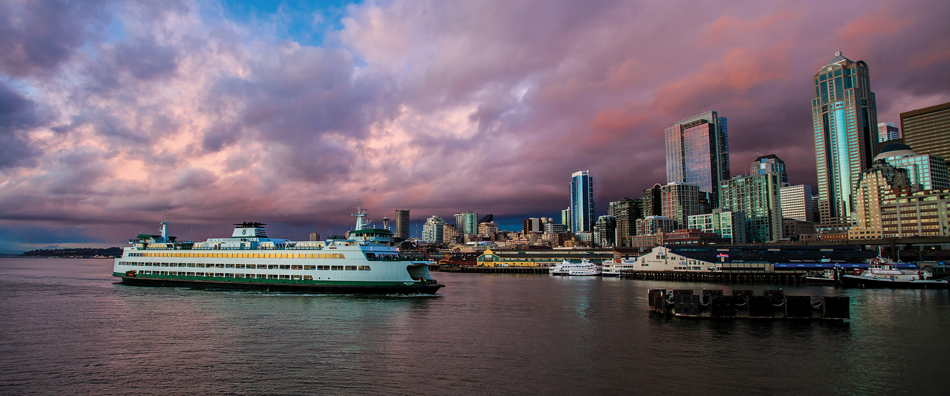 A ferry arriving in downtown Seattle, with pink and purple clouds in the sky